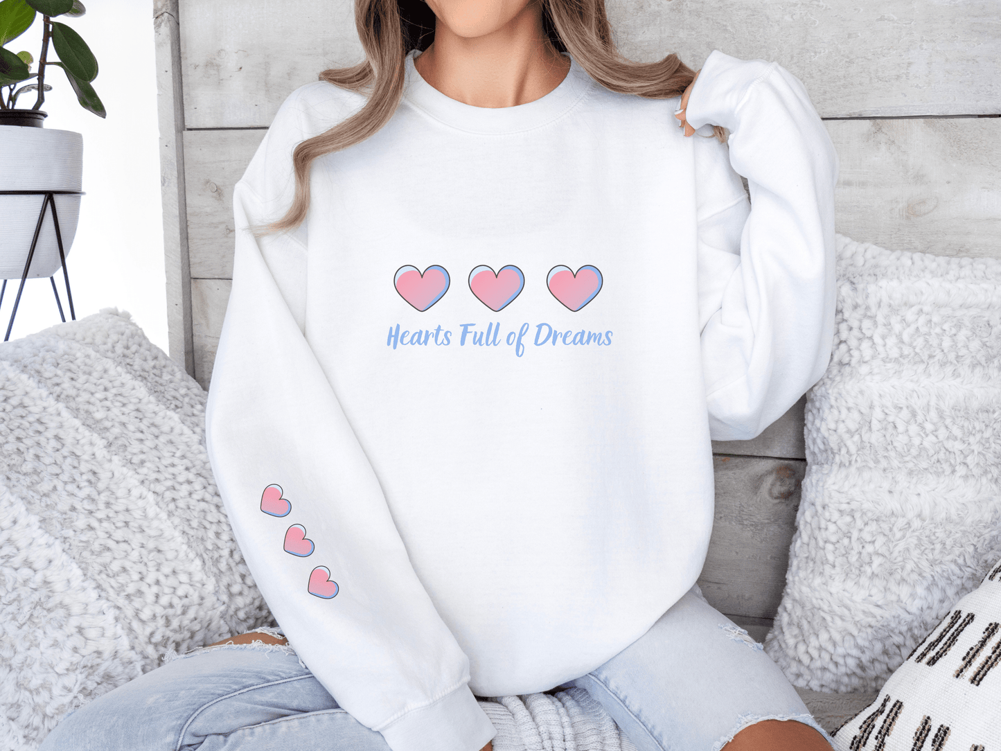 Woman wearing a white sweatshirt with pink heart illustrations and the phrase “Hearts Full of Dreams”