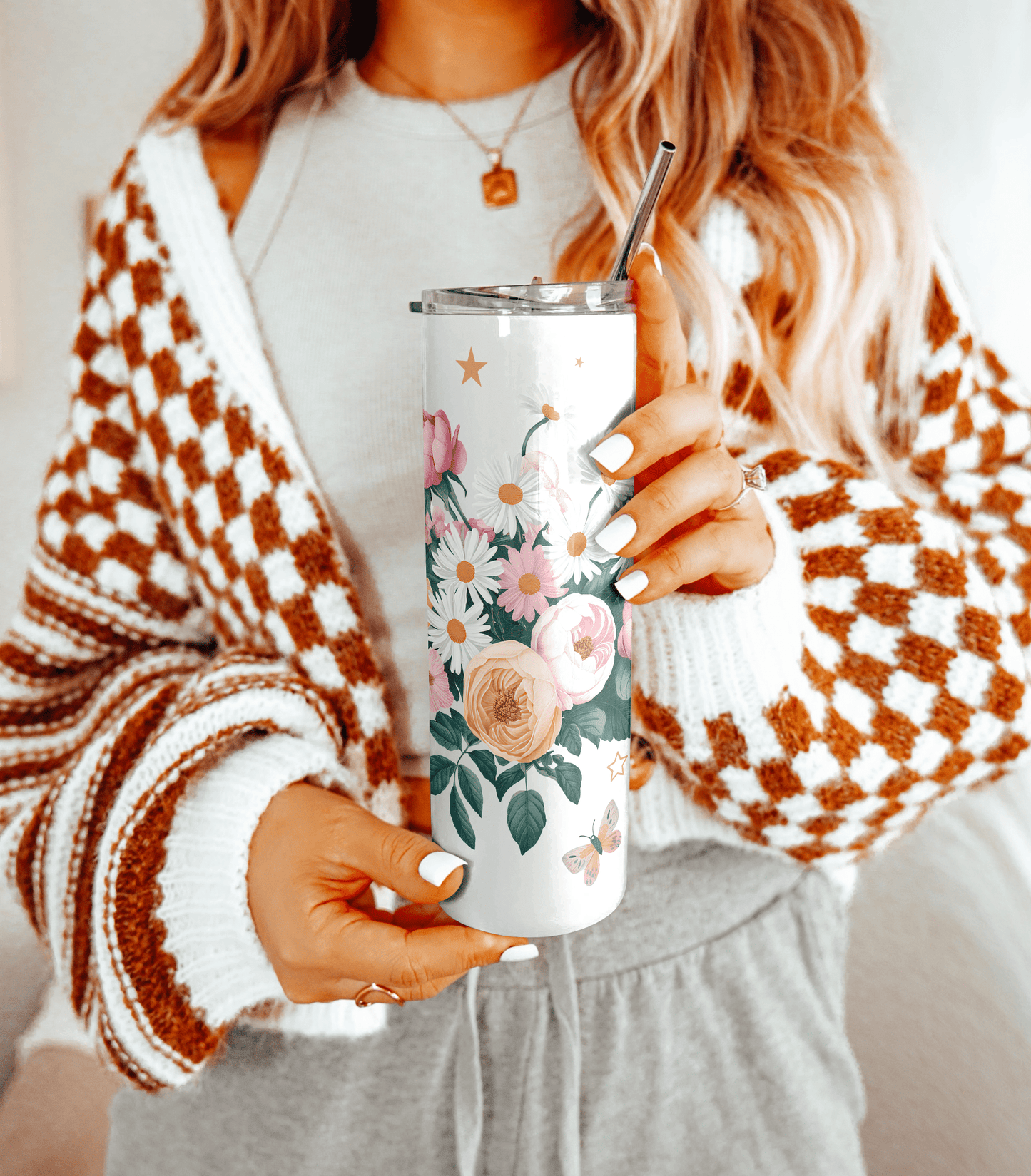 Woman holding floral tumbler with metal straw, wearing cozy sweater.