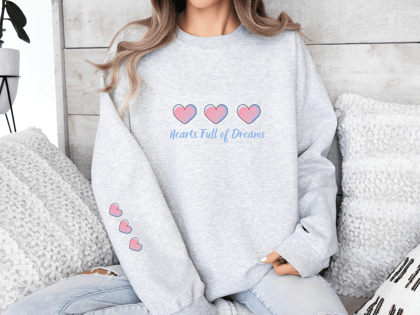 Woman wearing a ash grey sweatshirt with pink heart illustrations and the phrase “Hearts Full of Dreams”
