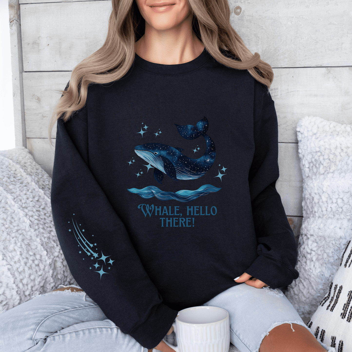 Woman wearing a black sweatshirt featuring a galaxy-style whale jumping from ocean waves with the quote “Whale, Hello There!”