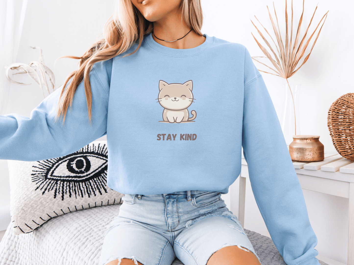 Woman wearing a light blue sweatshirt with a cute smiling cat and “Stay Kind” quote