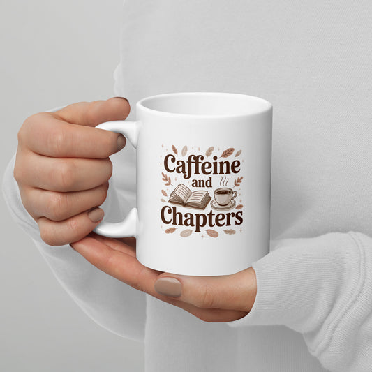 White mug with 'Caffeine and Chapters' text held by a hand on a light gray background