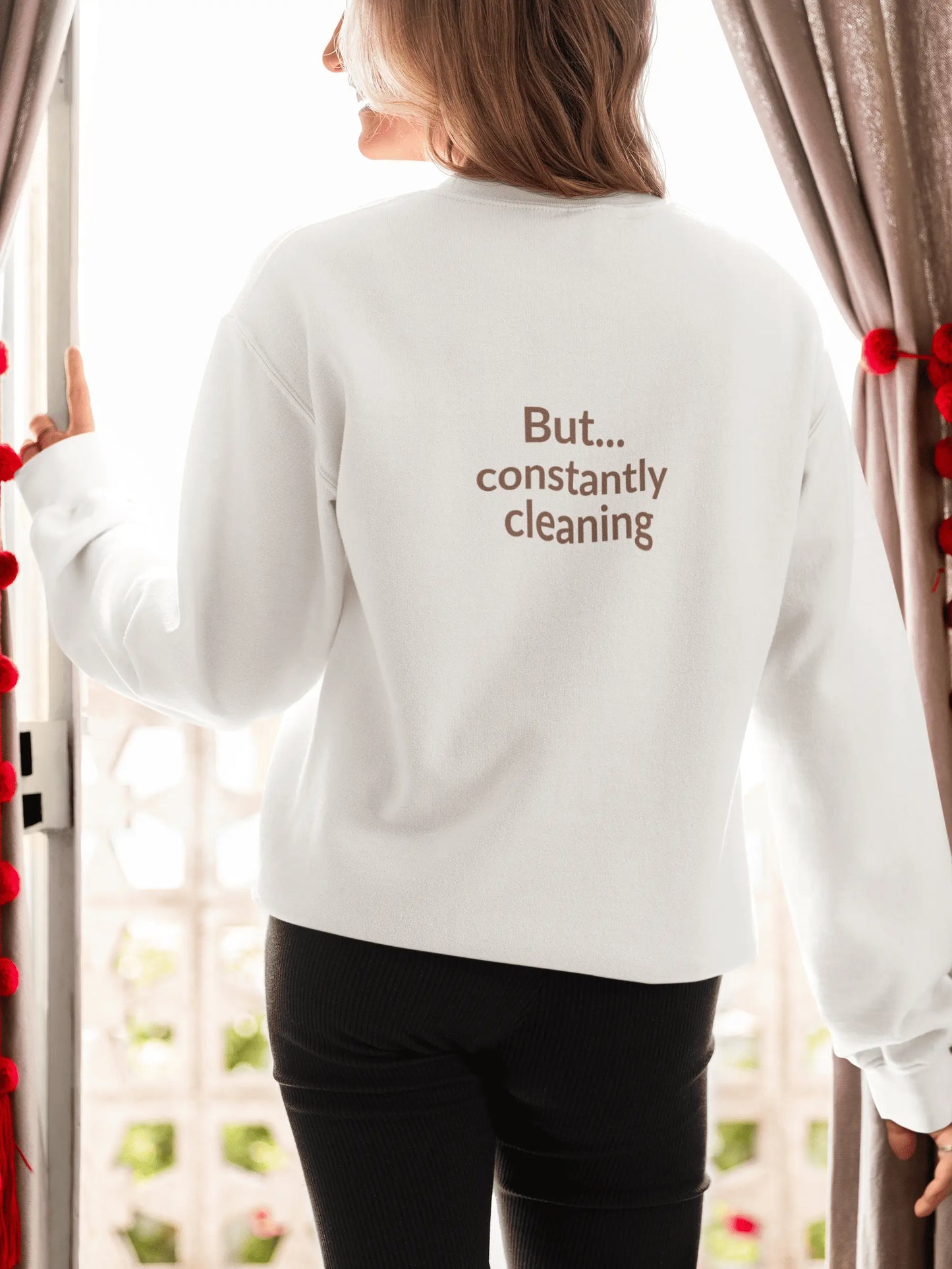 Person wearing a white sweatshirt with text "But..constantly cleaning" standing in front of a window.