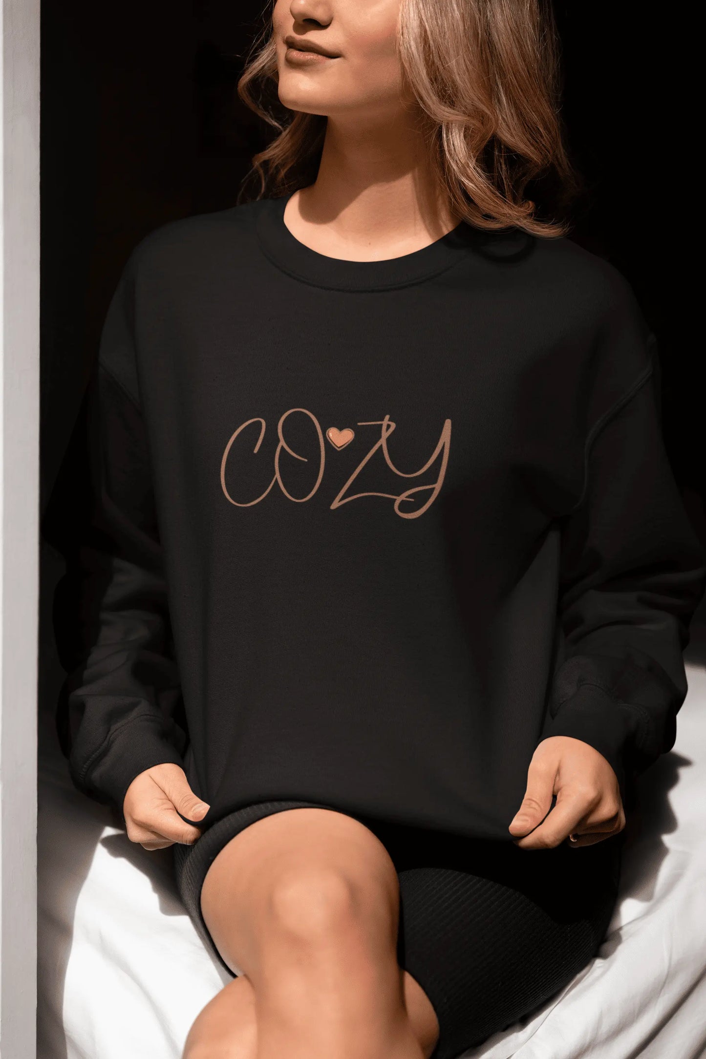 Person wearing a black sweatshirt with 'COZY' text sitting on a white surface.