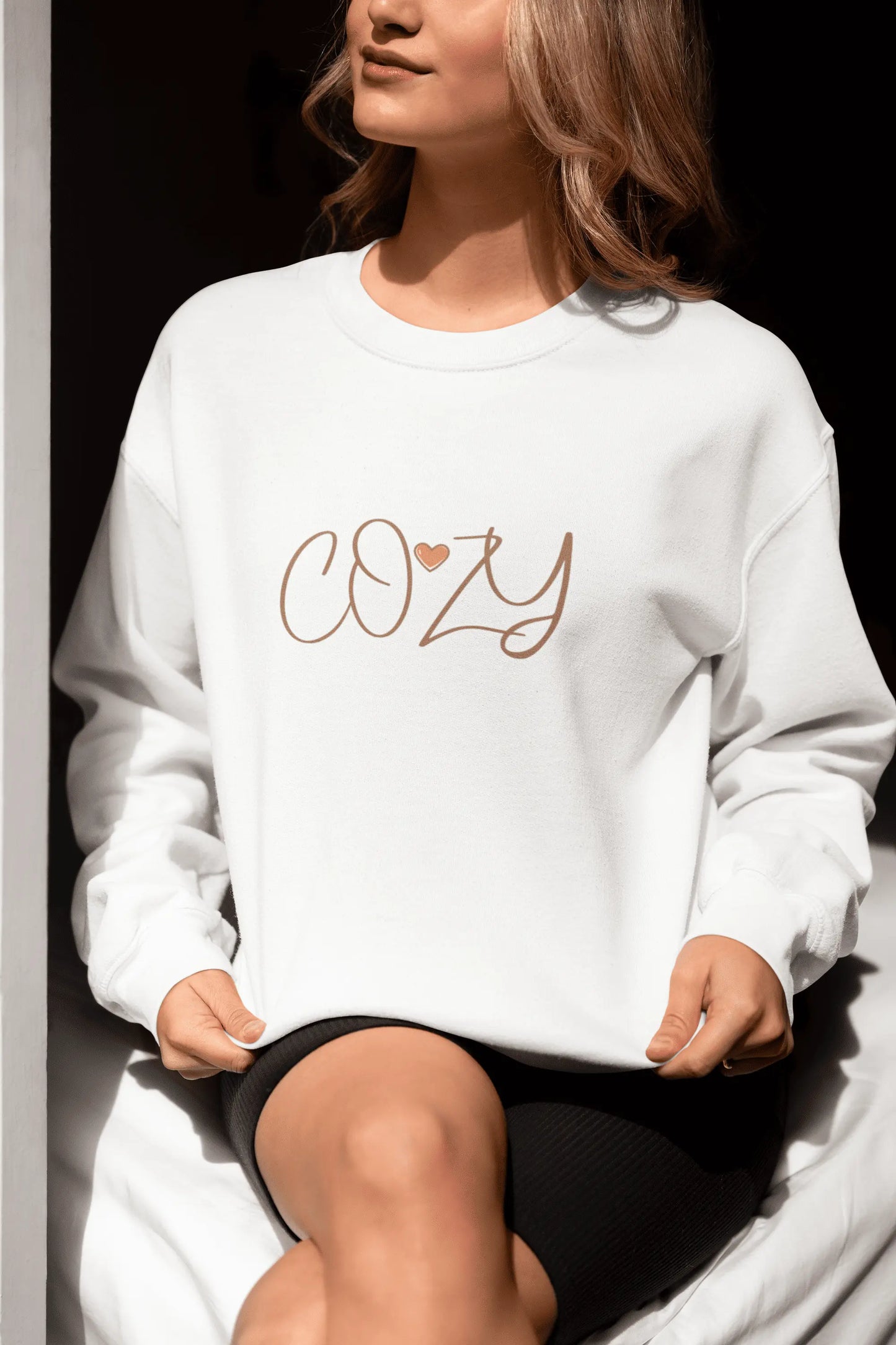 Person wearing a white sweatshirt with 'COZY' printed on it, sitting against a dark background.