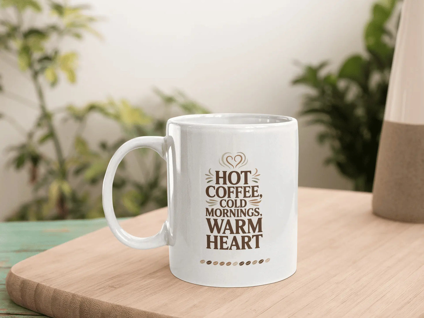 White mug with text 'Hot coffee, cold mornings, warm heart' on a wooden surface with plants in the background