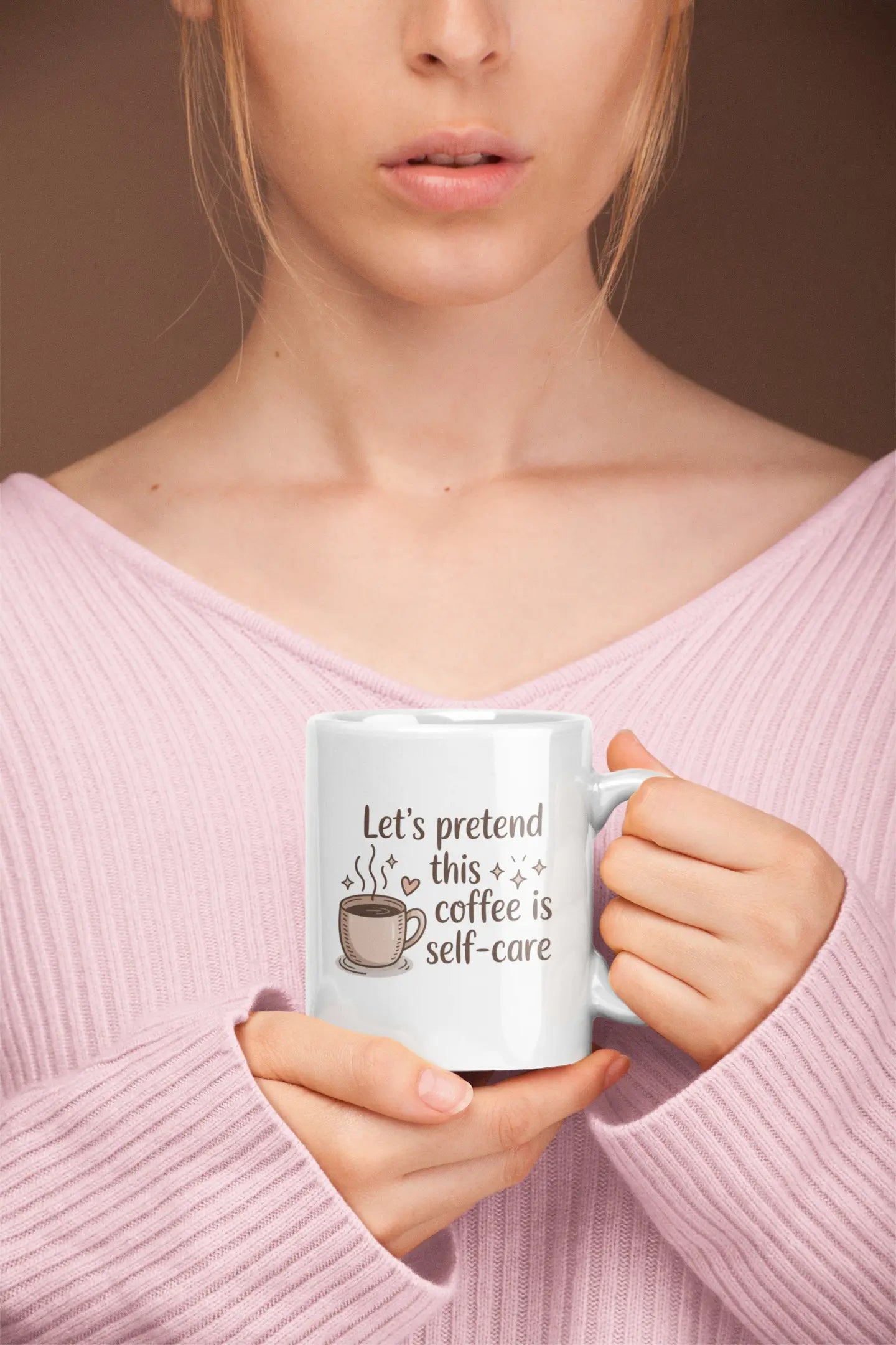 Person holding a mug with text 'Let's pretend this coffee is self-care' against a plain background