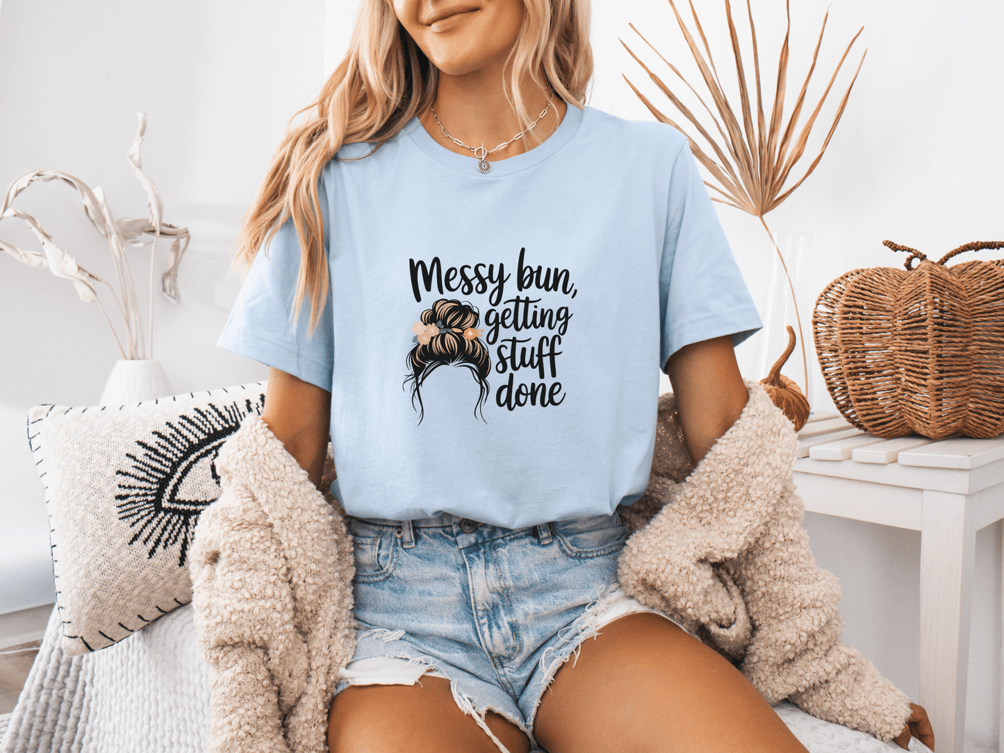 Woman wearing light blue “Messy Bun, Getting Stuff Done” t-shirt, posing casually on a bed.