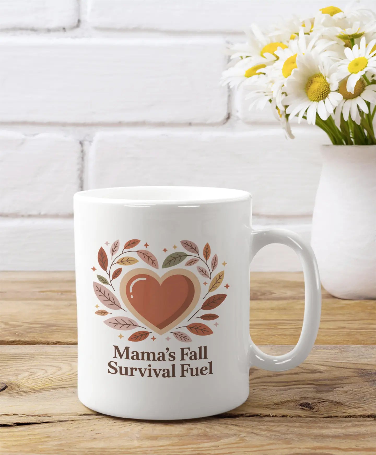 White mug with 'Mama's Fall Survival Fuel' design on a wooden surface with flowers in the background.