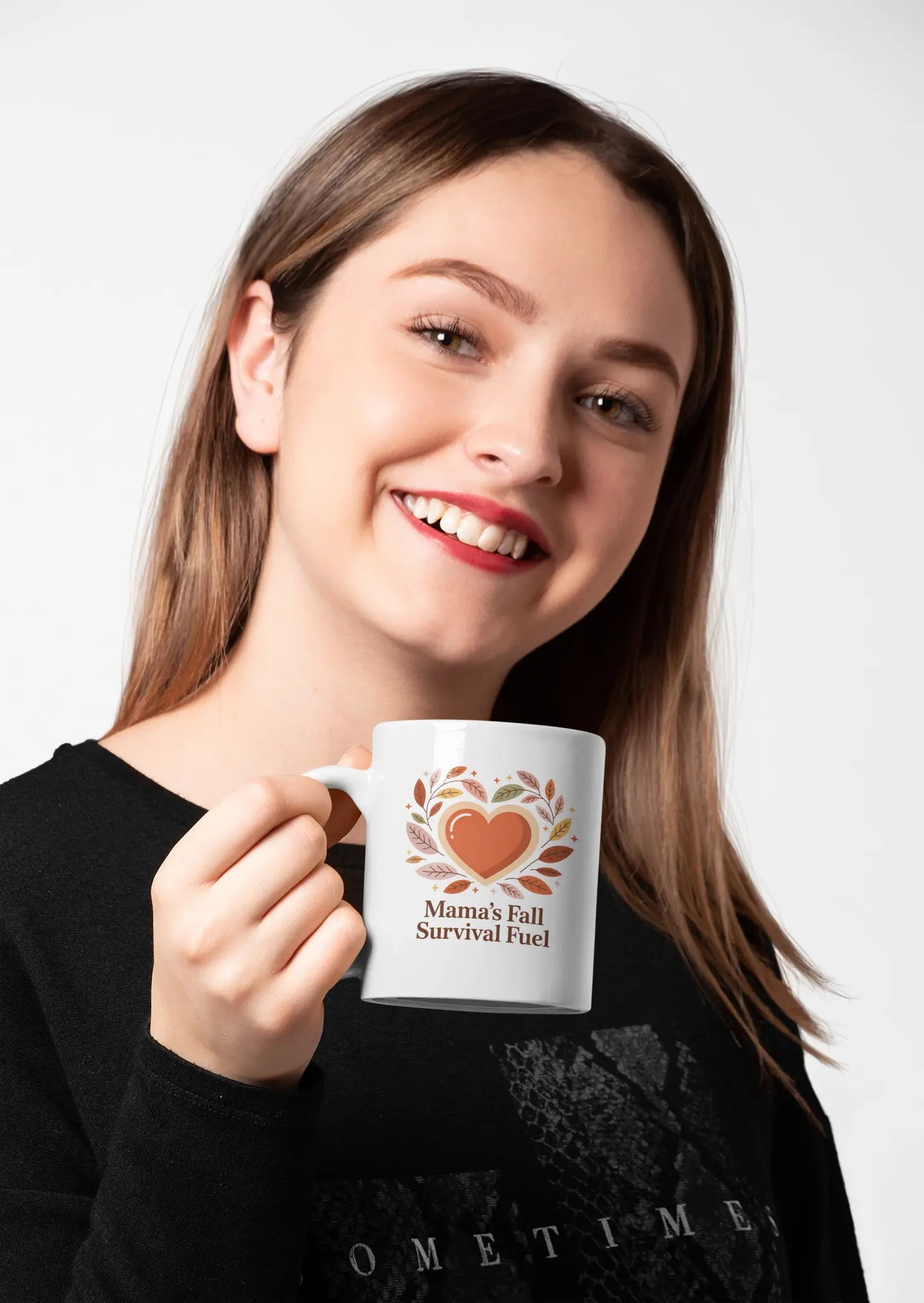 Woman holding a mug with a heart design and text "Mama's Fall Survival Fuel" on a white background