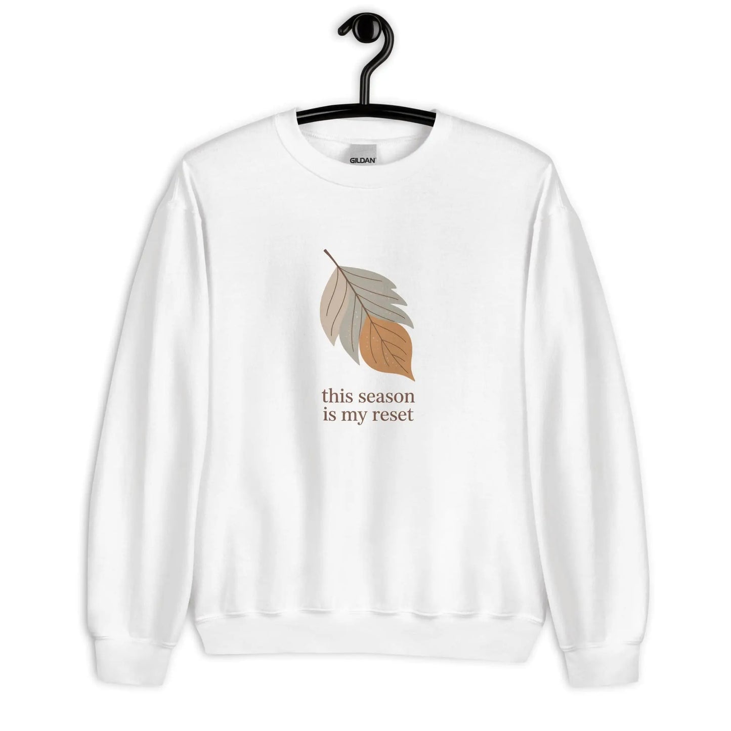 White sweatshirt with leaf graphic and text 'this season is my reset' on a hanger against a white background