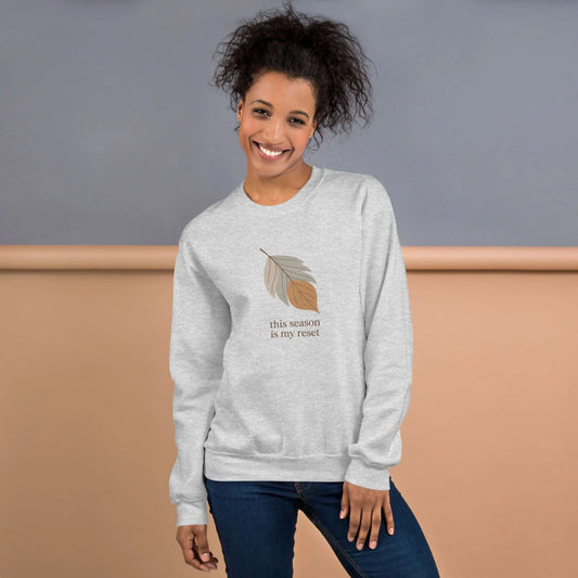 Person wearing a gray sweatshirt with a leaf design and text "this season is my reset" against a gradient background