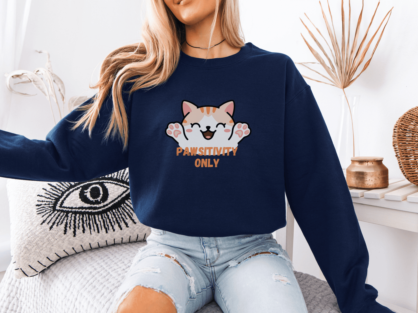 Woman wearing a navy blue sweatshirt with a cheerful orange kitten and the phrase “Pawsitivity Only,” seated in a cozy room