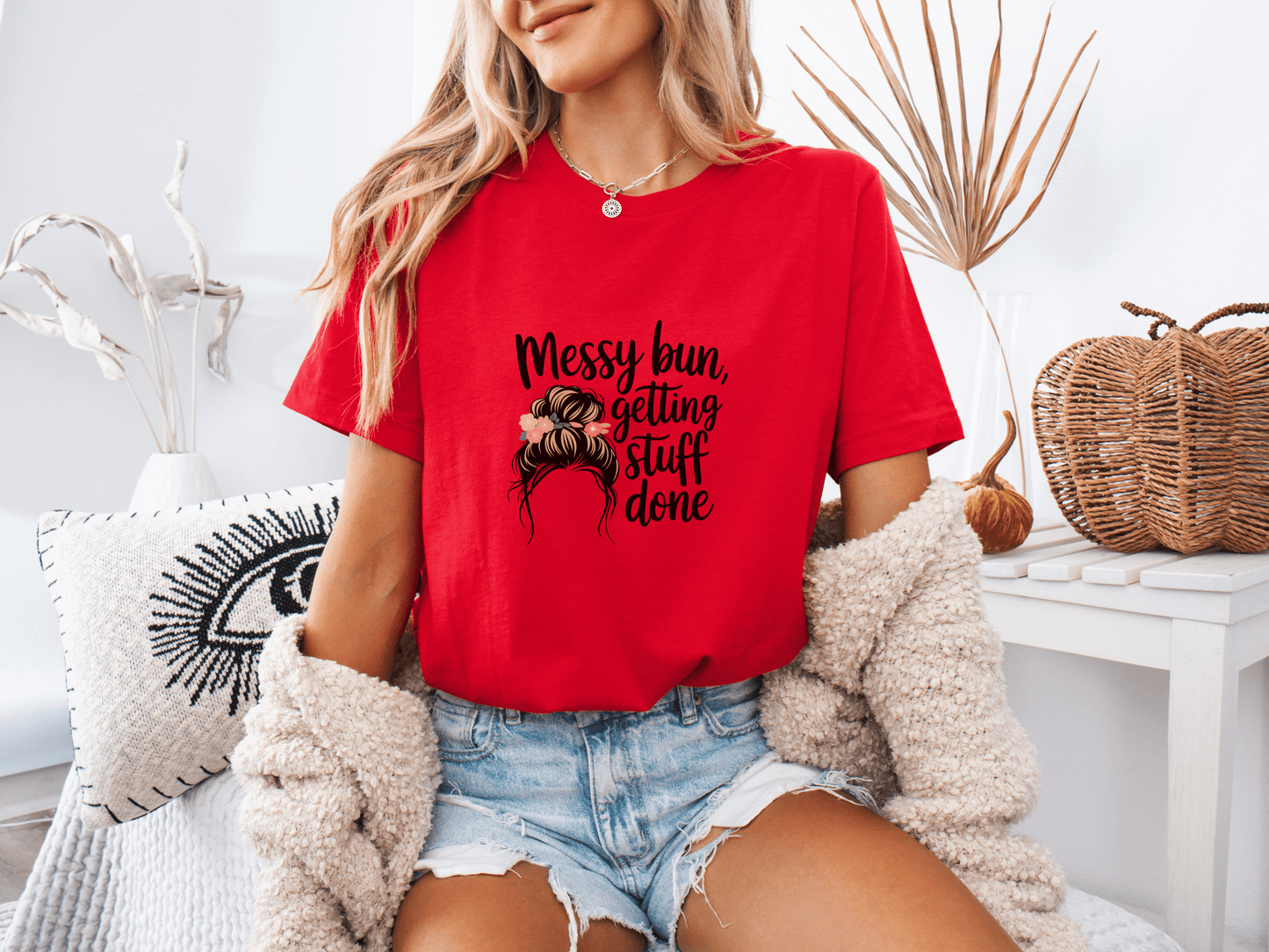 Woman wearing red “Messy Bun, Getting Stuff Done” t-shirt, posing casually on a bed.