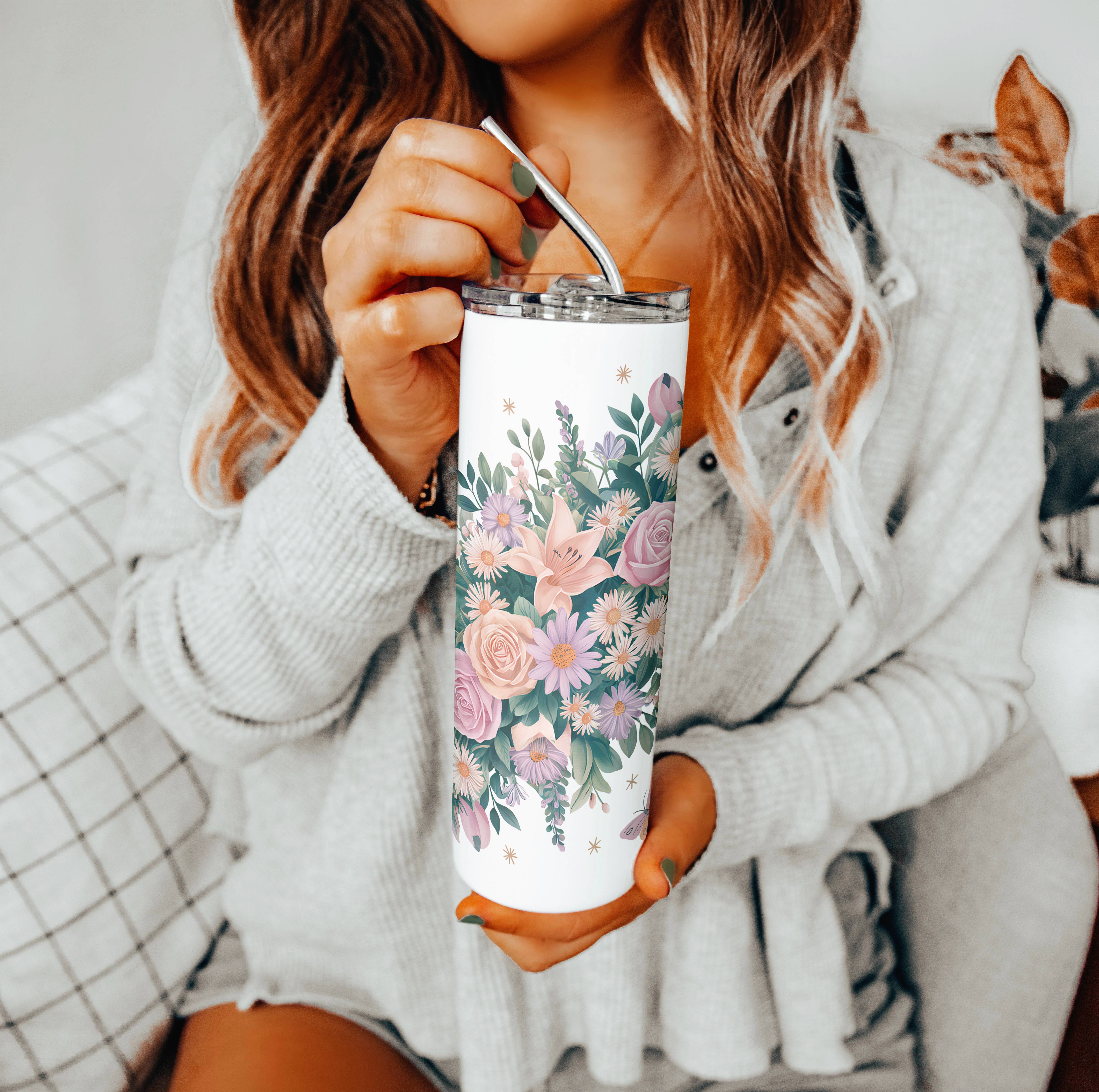 Woman in a cozy grey sweater holding a white stainless steel tumbler decorated with pink and purple wildflowers and green leaves, featuring a metal straw.