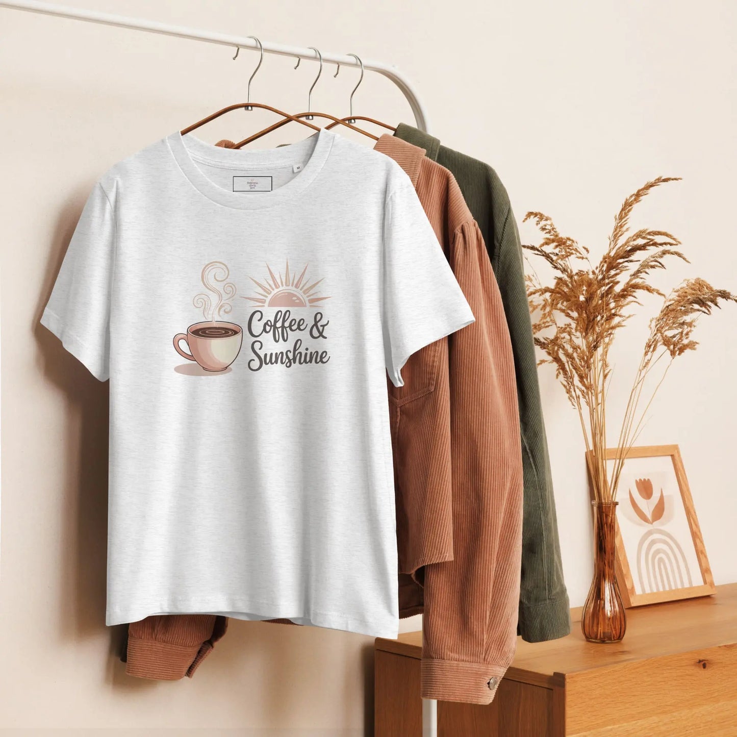 Heather grey organic mom shirt hanging on a wooden hanger, styled with neutral-toned jackets. “Coffee & Sunshine” print.