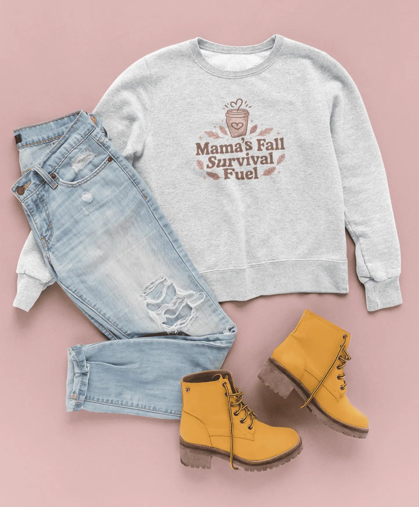 Gray sweatshirt with text "Mama's fall survival fuel", light blue jeans, and yellow boots on a pink background