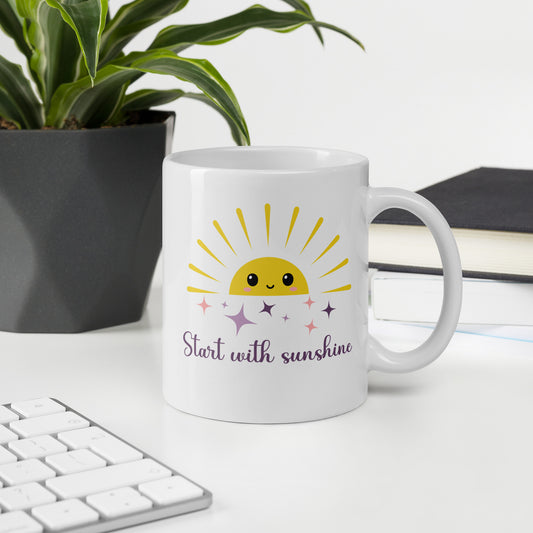 White mug with pastel sun and sparkles on a desk beside a plant and keyboard — cheerful morning coffee cup for moms who love sunshine vibes.