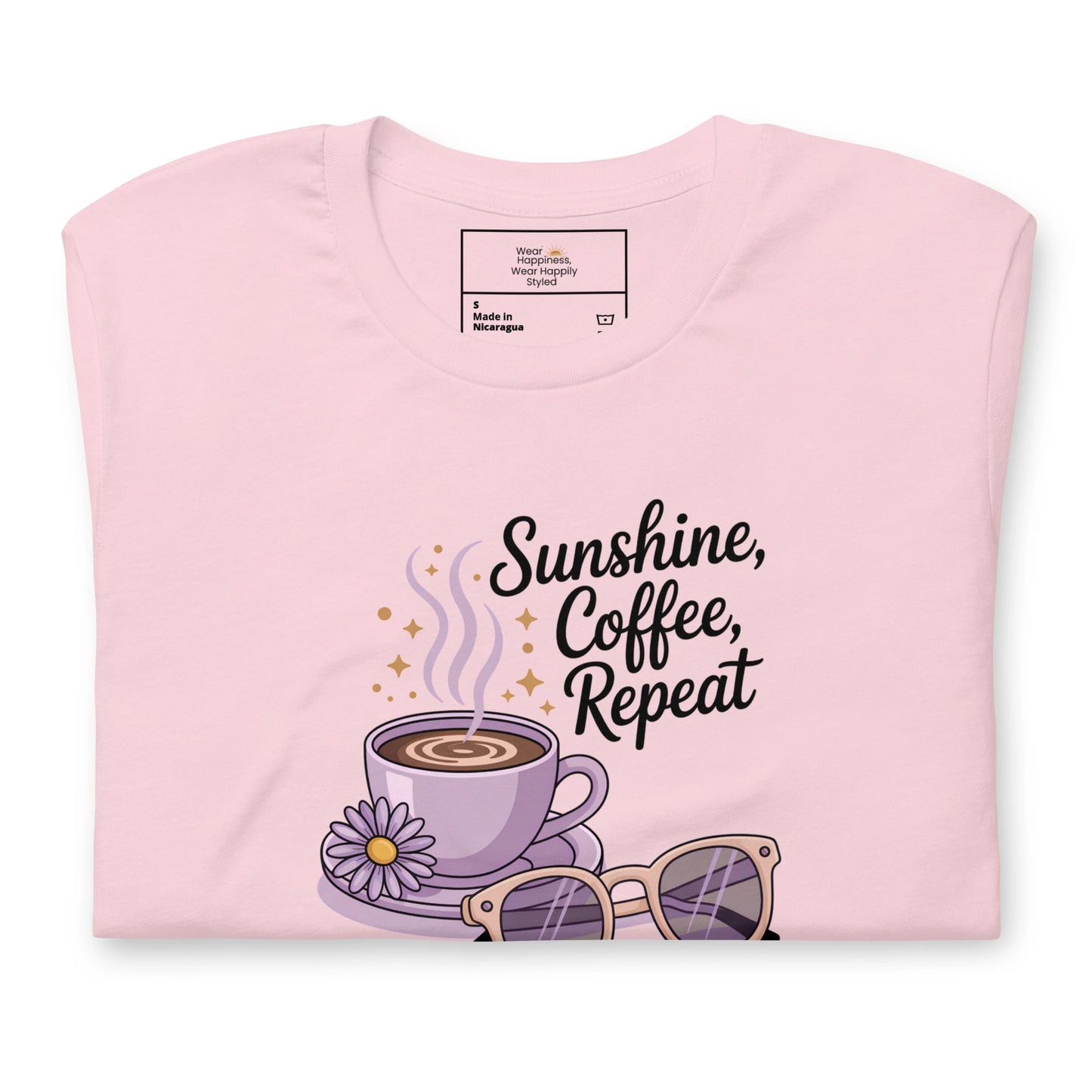 Folded pink t-shirt showing close-up of “Sunshine, Coffee, Repeat” graphic with pastel latte art, sunglasses and sparkles