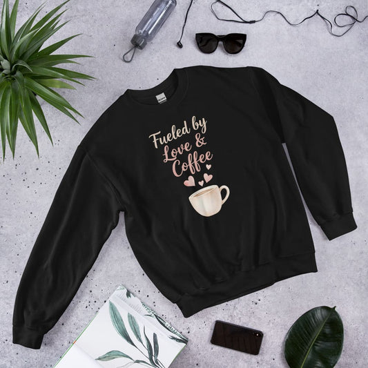 Black sweatshirt with 'Fueled by Love & Coffee' text and coffee cup graphic on a gray surface with accessories.