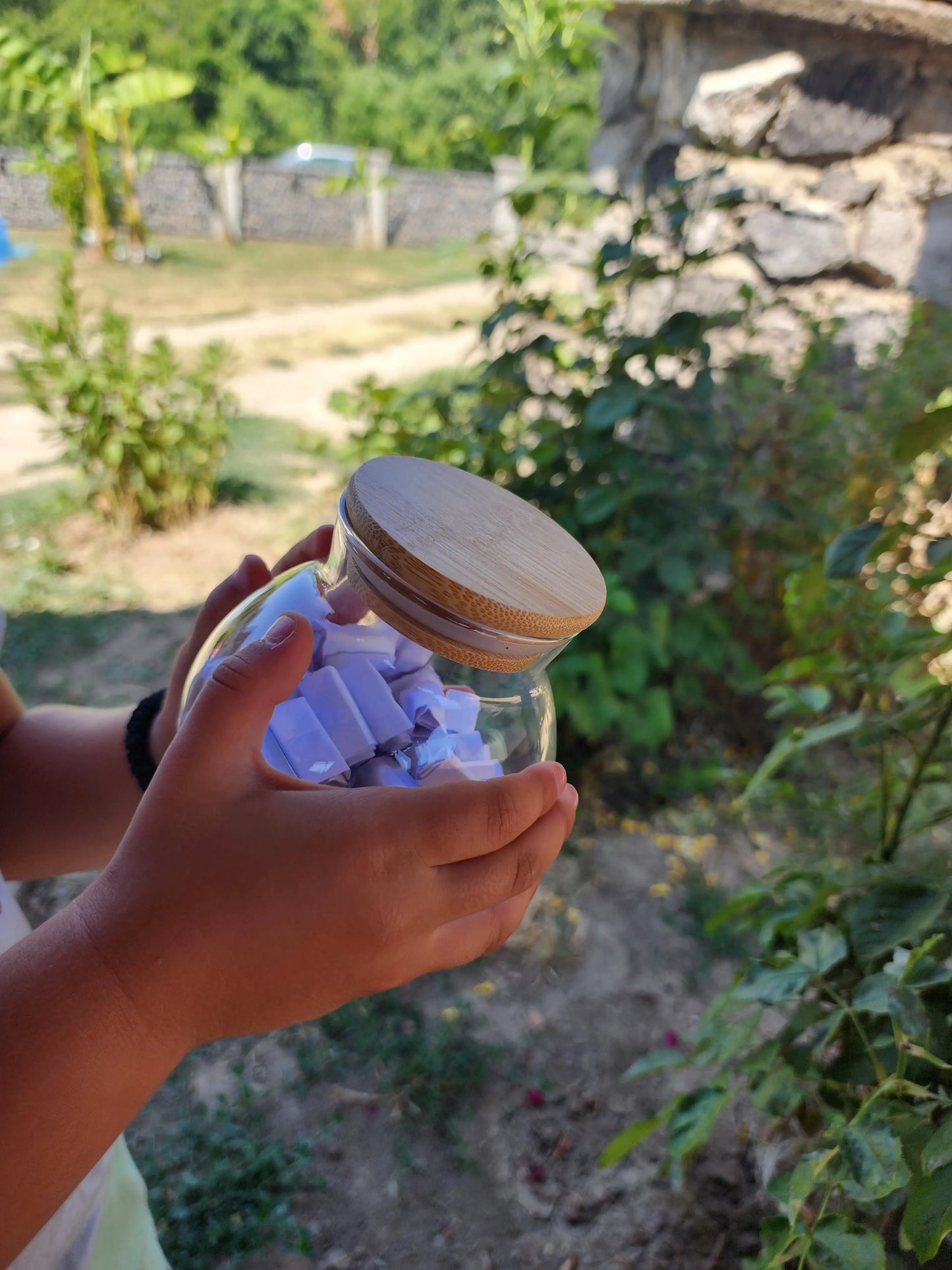 Child’s hands holding a small glass jar filled with rolled paper activity prompts