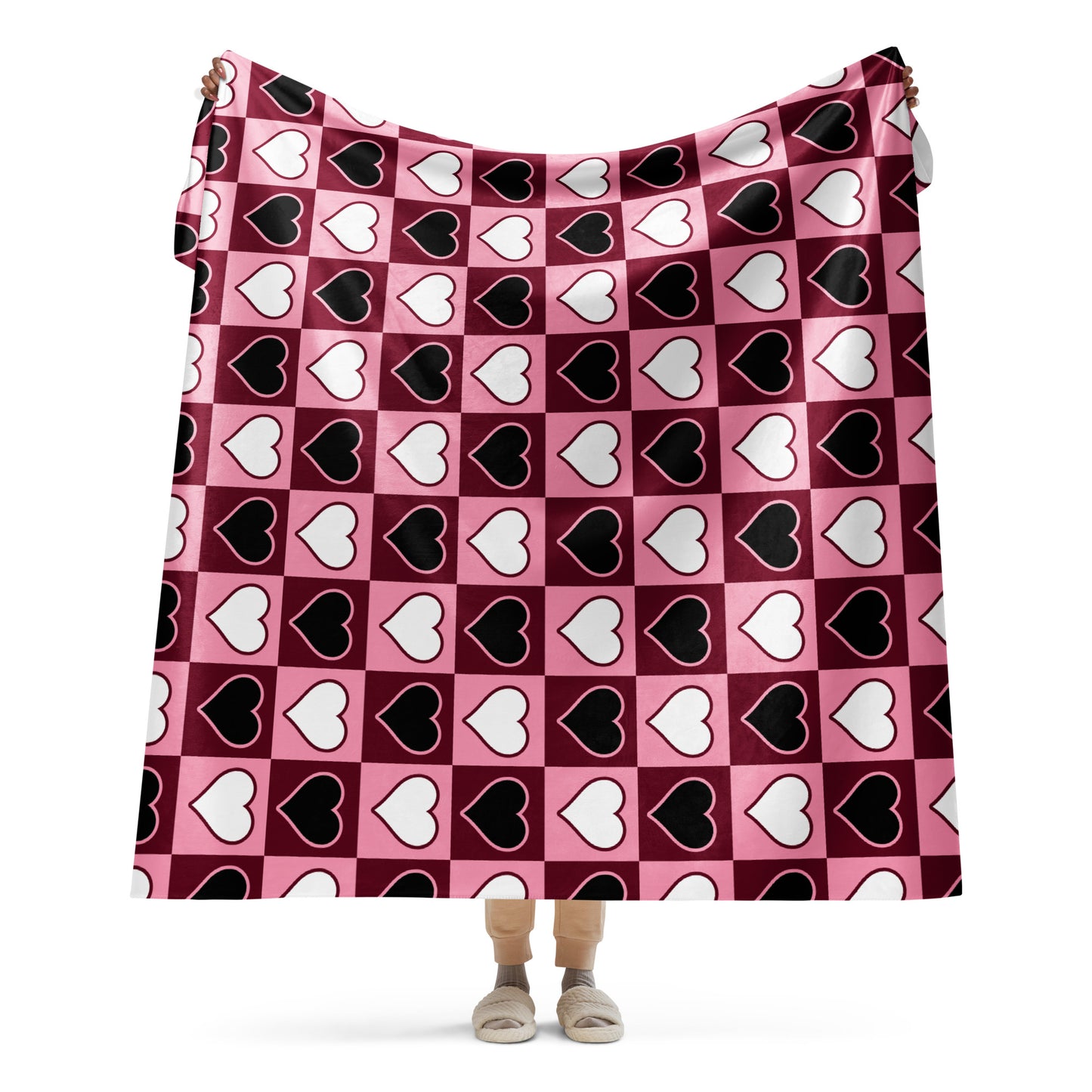 Full view of large heart pattern sherpa blanket held up by a person, showing the full design in pink, white, and black