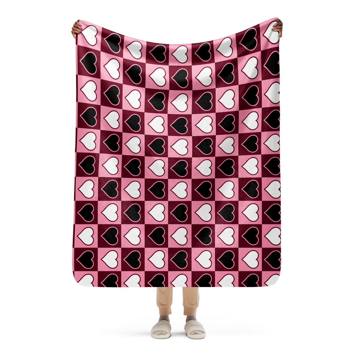 Full view of medium heart pattern sherpa blanket held up by a person, showing the full design in pink, white, and black