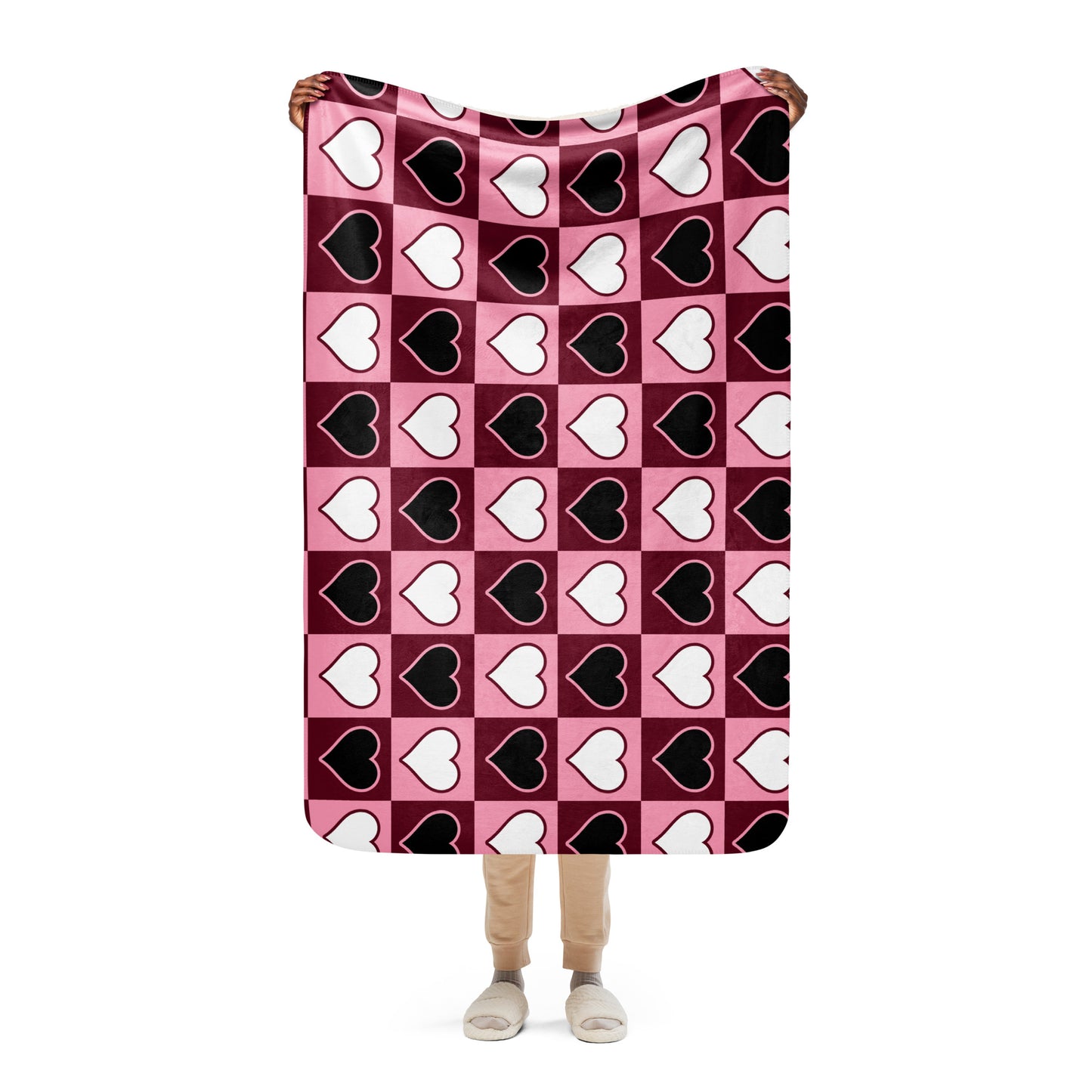 Full view of small heart pattern sherpa blanket held up by a person, showing the full design in pink, white, and black