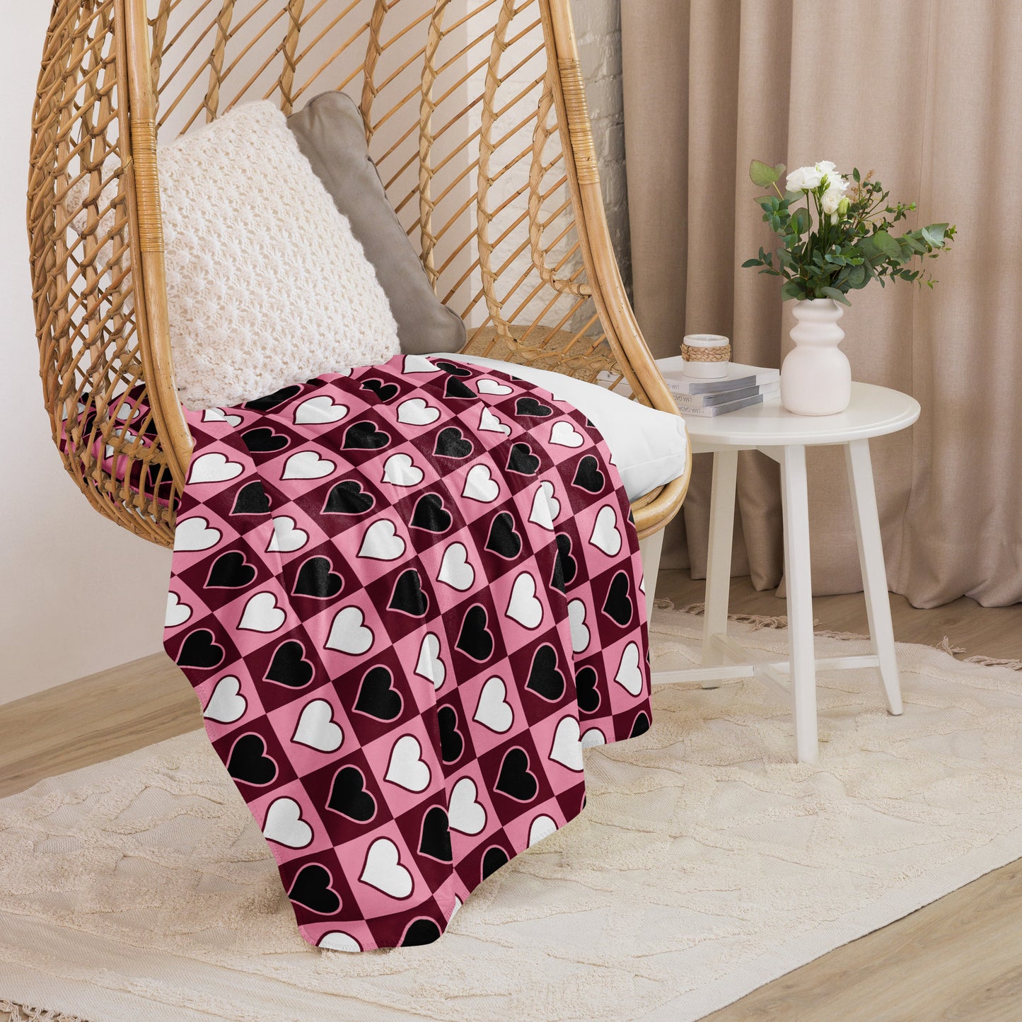 Medium size heart design throw blanket in pink tones, draped over a hanging rattan chair