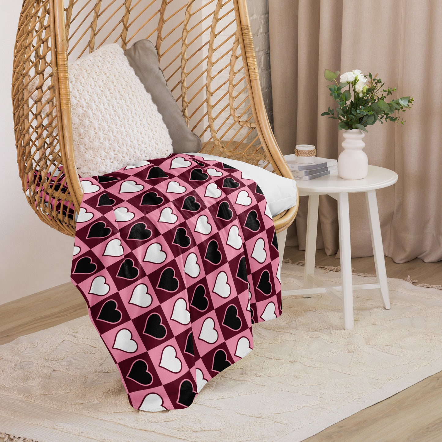 Small size heart pattern throw blanket in pink, black, and white, folded over a cozy rattan hanging chair