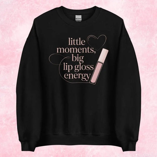 Black sweatshirt with 'little moments, big lip gloss energy' text and lip gloss graphic on a pink background