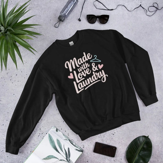 Black sweatshirt with 'Made with Love & Laundry' text on a gray surface with plants and accessories.