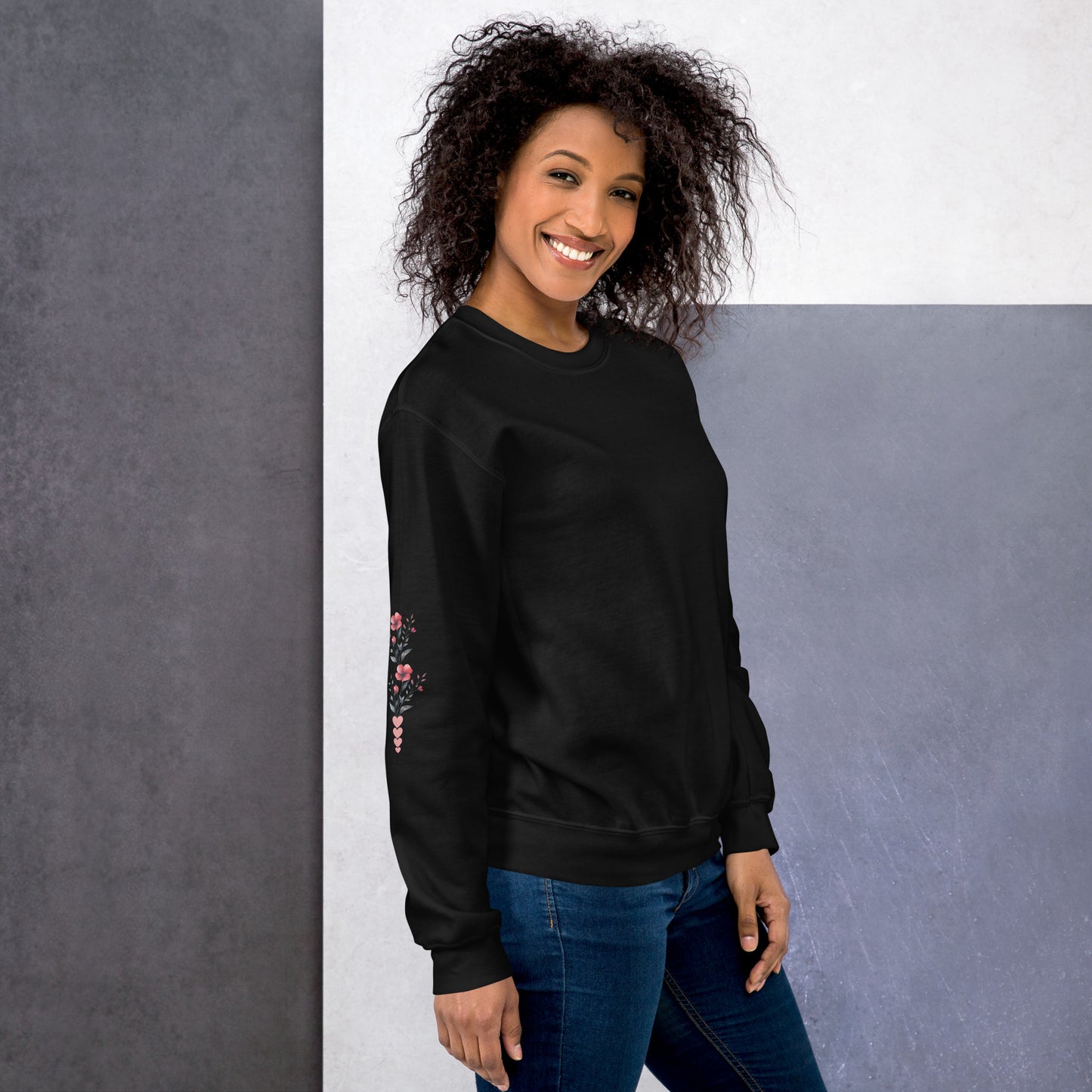 Smiling woman wearing black sweatshirt with floral design detail on the sleeve - right view