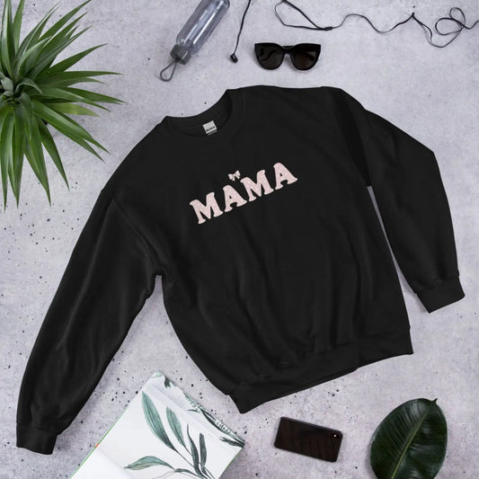 Black sweatshirt with 'MAMA' text on a gray surface with accessories around