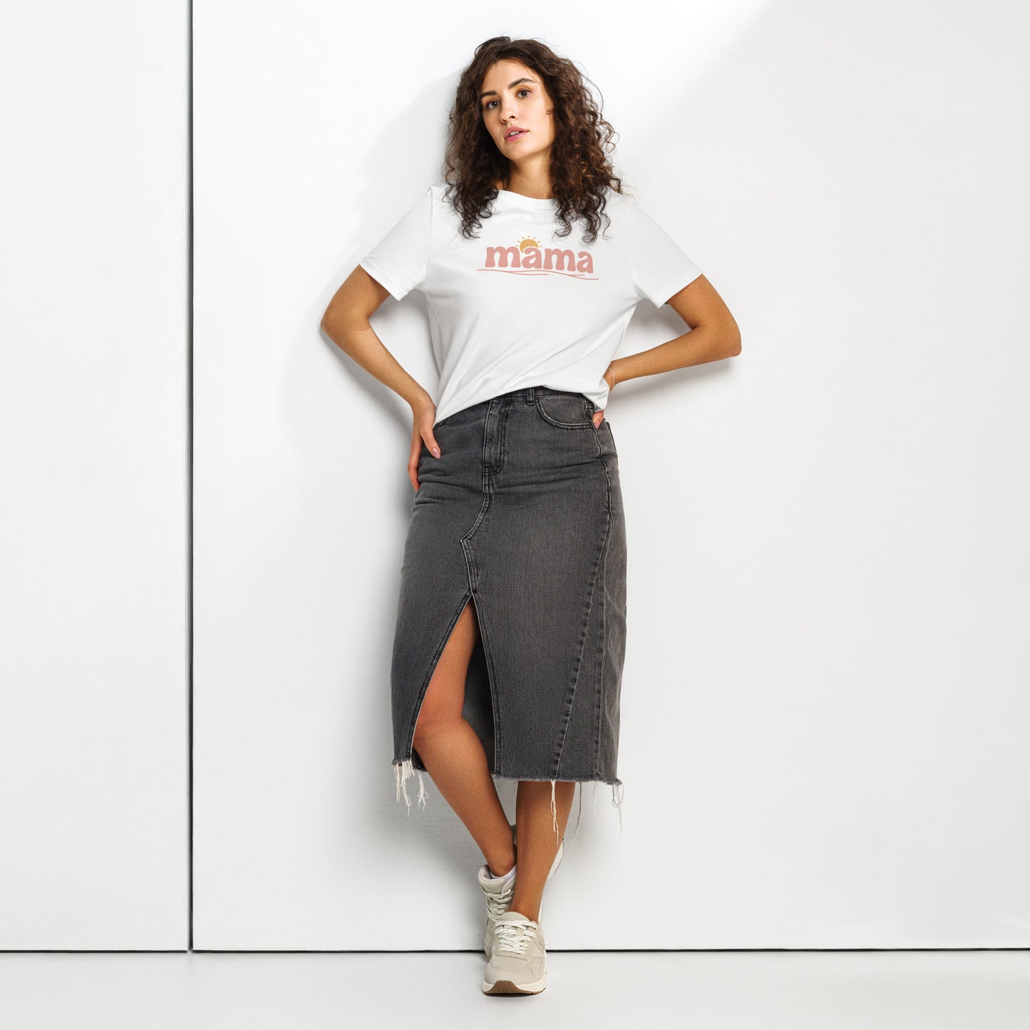 Woman wearing white ‘mama’ t-shirt with pastel sun design, styled with denim skirt, standing against white wall