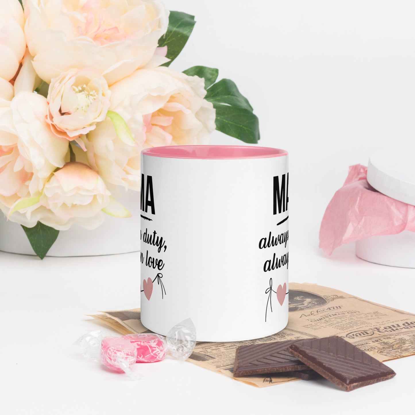 White ceramic mug with pink handle and inner color – “MAMA always on duty, always in love” quote with heart design, styled with chocolate and flowers - back view