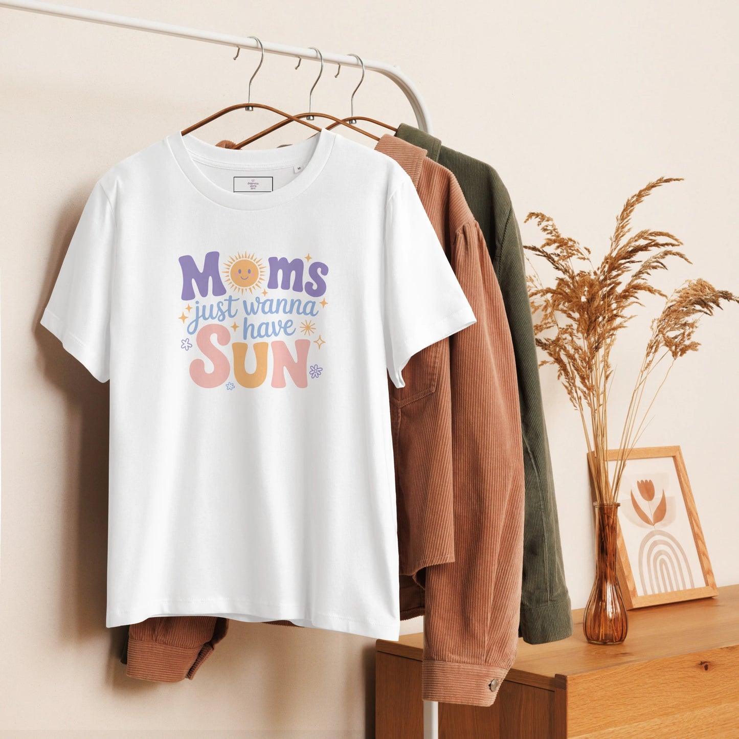 White t-shirt with “Moms Just Wanna Have Sun” pastel design hanging on clothing rack – cozy styled product photo for summer t-shirt for moms