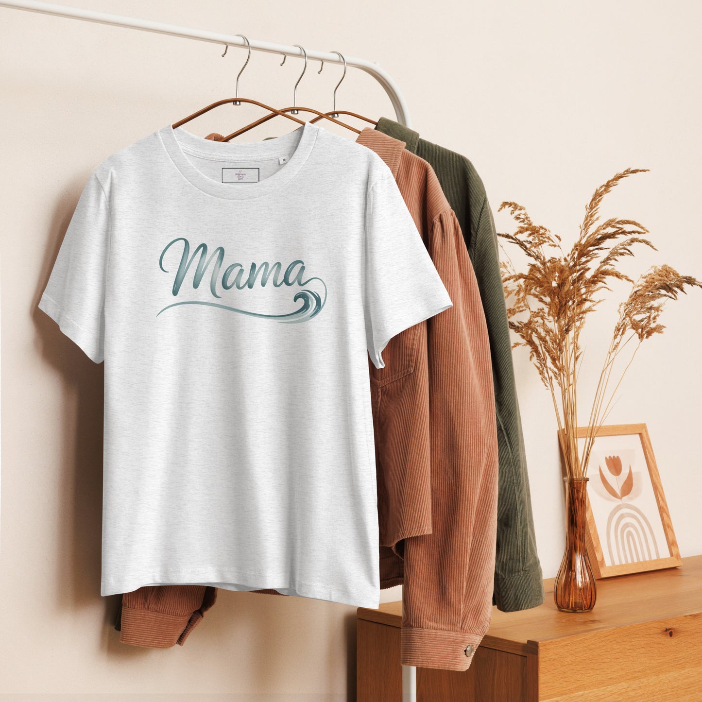 Grey Ocean Mama t-shirt with wave lettering hanging on clothing rack, styled with cozy summer tones
