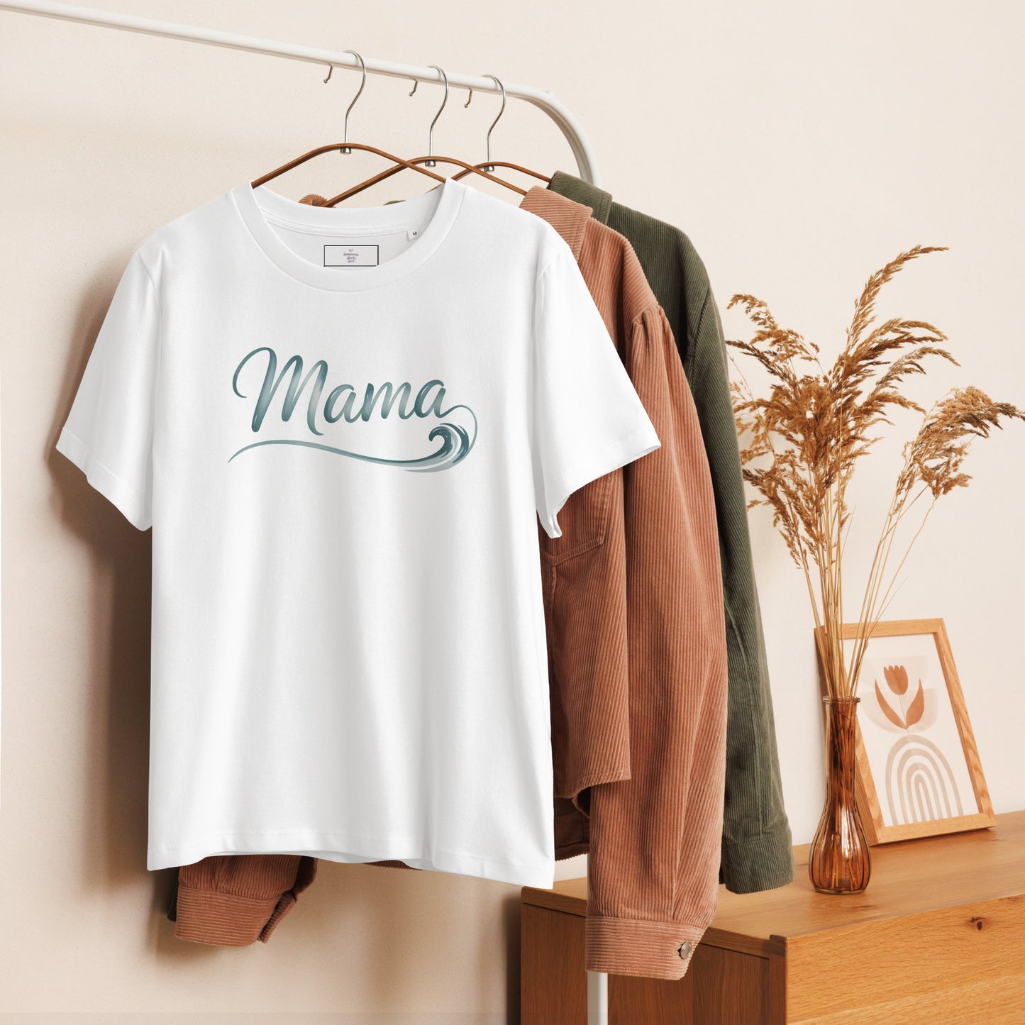 White Ocean Mama t-shirt with wave lettering hanging on clothing rack, styled with cozy summer tones