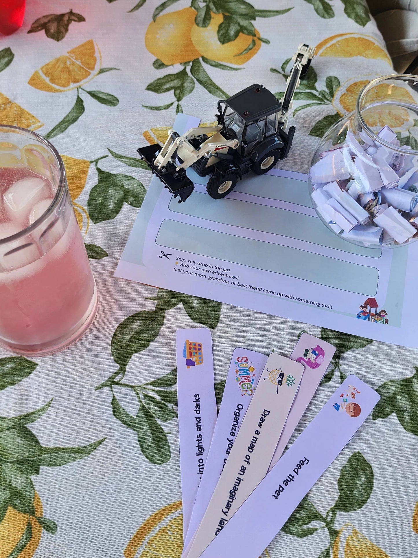 Printable activity strips and a filled glass jar on a table with a toy tractor and pink drink