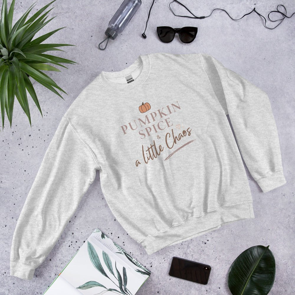 White sweatshirt with 'Pumpkin Spice & a Little Chaos' text on a gray surface with accessories.