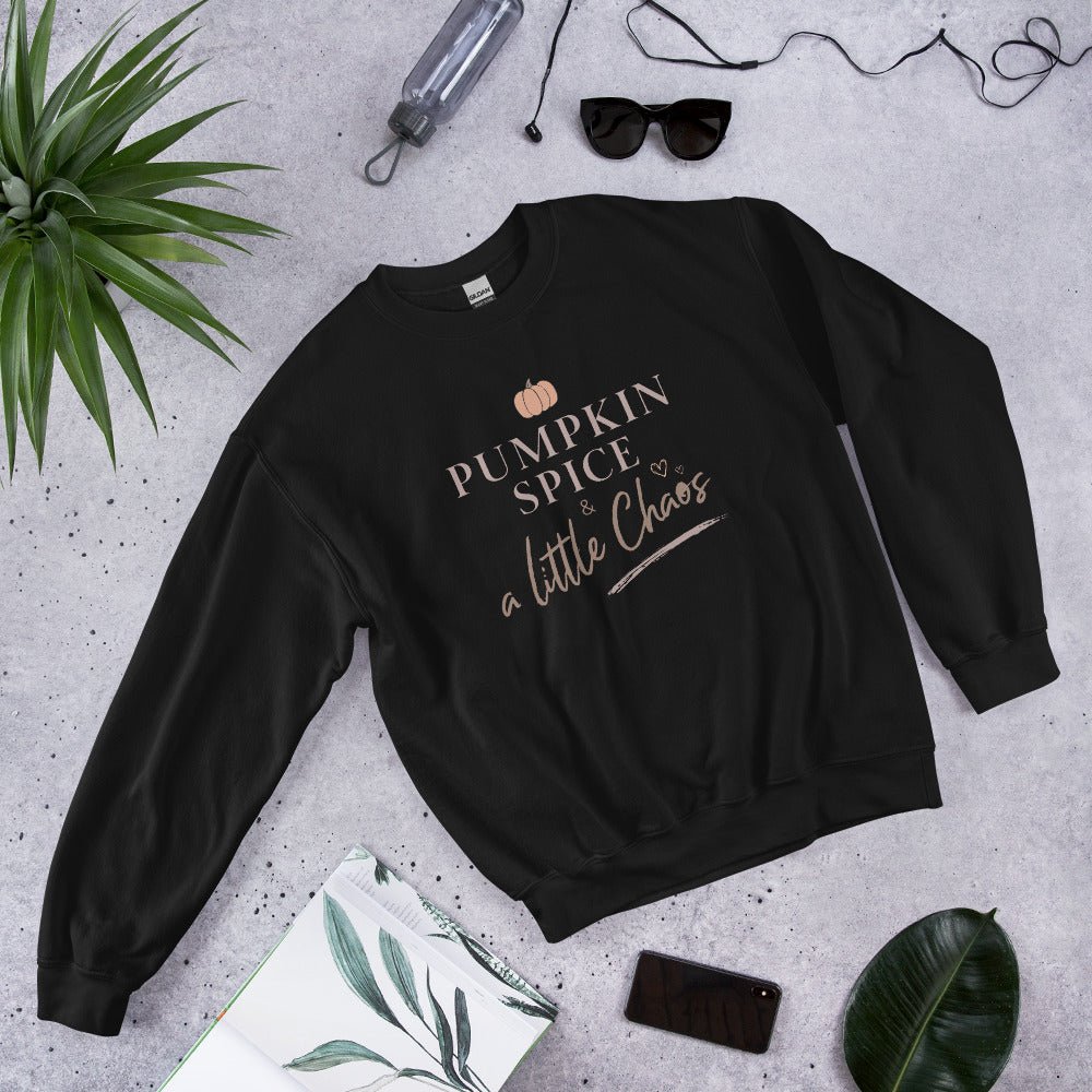 Black sweatshirt with 'Pumpkin Spice & a Little Chaos' text on a gray surface with accessories.