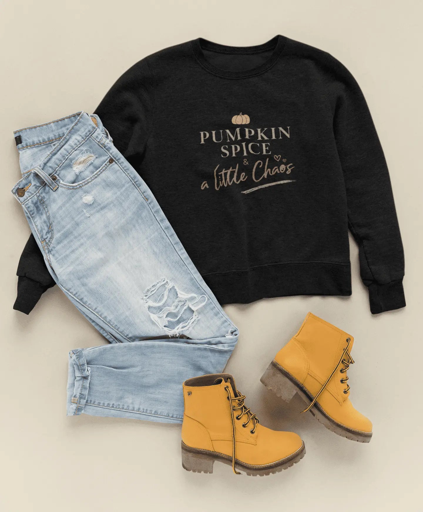 Black sweatshirt with text "Pumpkin spice & a little chaos", light blue jeans, and yellow boots on a beige background