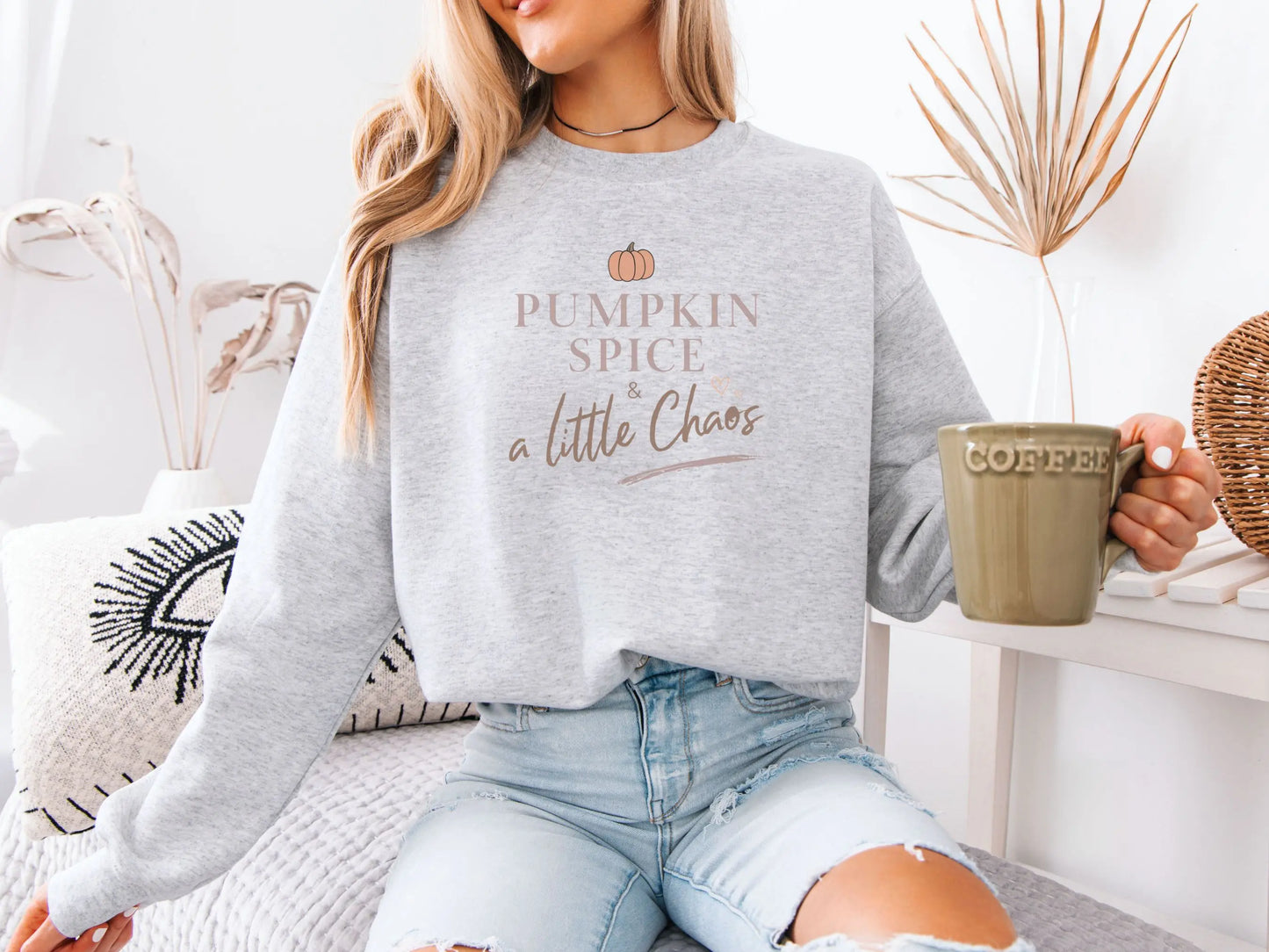Person wearing a gray sweatshirt with 'Pumpkin Spice & a Little Chaos' text, holding a coffee mug.