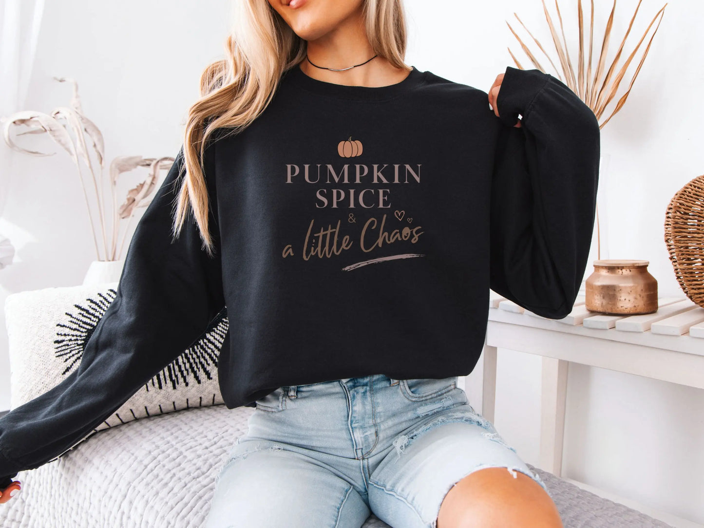Person wearing a black sweatshirt with 'Pumpkin Spice & a Little Chaos' text, sitting on a couch.