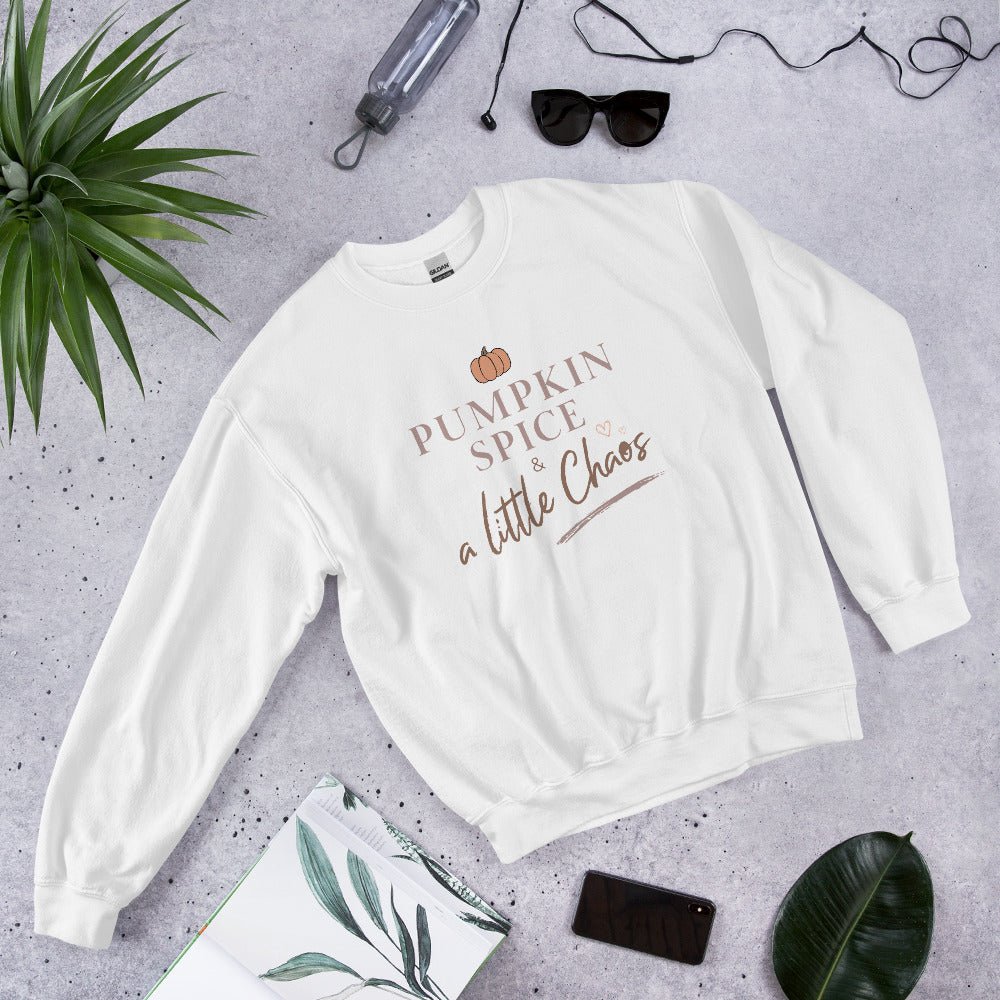 White sweatshirt with 'Pumpkin Spice & a Little Chaos' text on a gray surface with accessories.