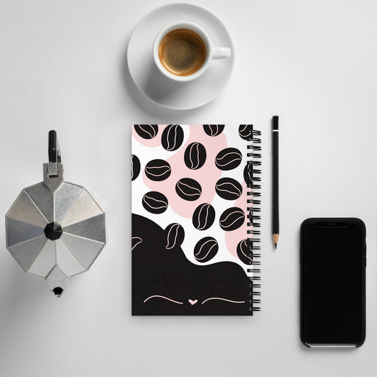 Flat lay of a “Coffee Lover” spiral notebook with black and pink coffee bean design, placed on a white desk alongside an espresso cup, moka pot, pencil, and smartphone — back of the notebook.