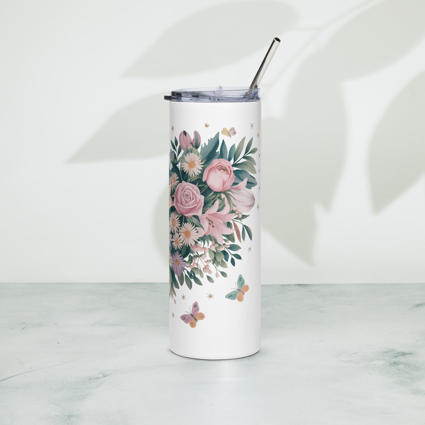 White stainless steel tumbler with detailed pink floral and greenery illustration, metal straw, and clear lid. Positioned upright on a light surface with soft leaf shadows in the background.