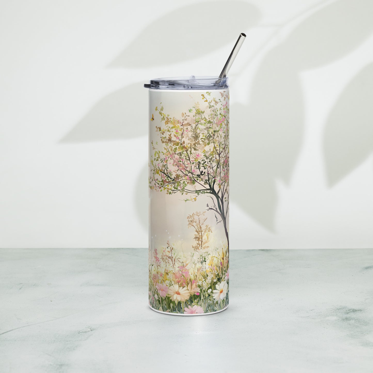 Stainless steel tumbler with pastel floral tree design, placed on a light surface with soft leaf shadows in the background.