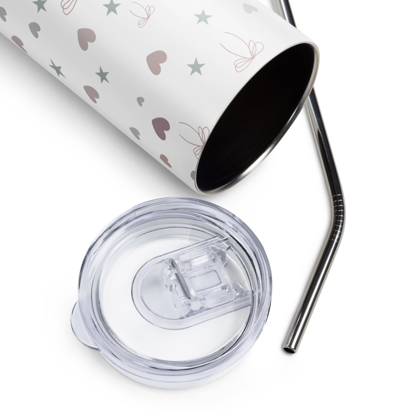 Stainless steel tumbler with pastel hearts, stars, and bows lying on its side, next to a metal straw and clear lid.